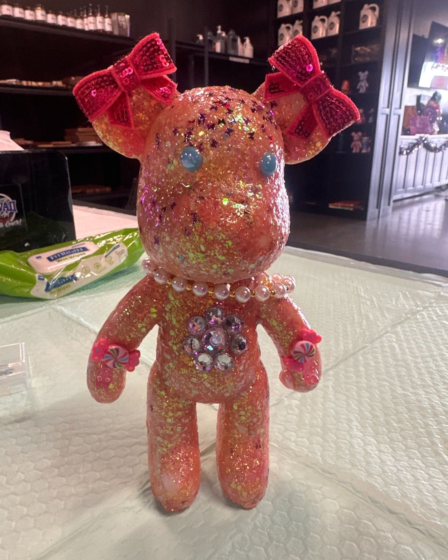 Sparkly pink beaded figurine with large bows standing on a table in a shop.