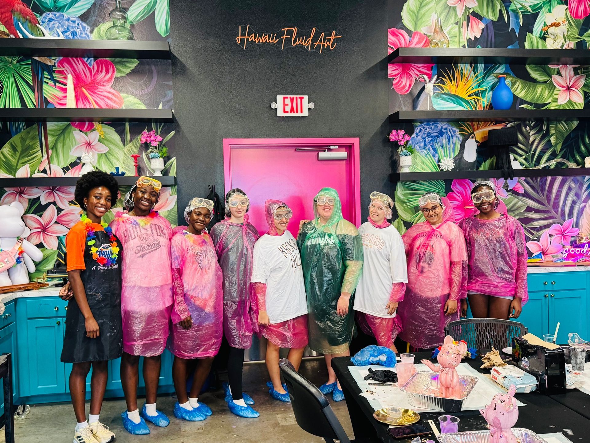 Group of people in colorful plastic covers posing in front of a pink door and floral wall display