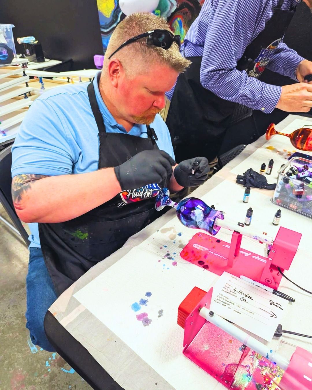 Person in blue shirt and apron carefully assembling parts at a table with pink and purple items.