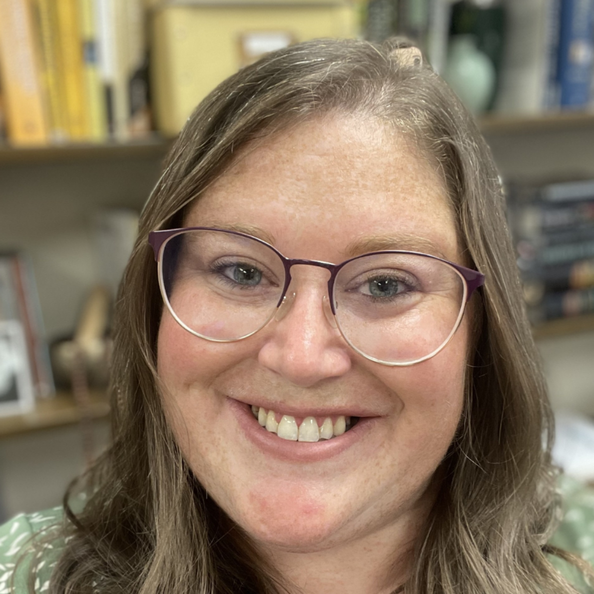 Smiling person with glasses in a softly blurred indoor setting