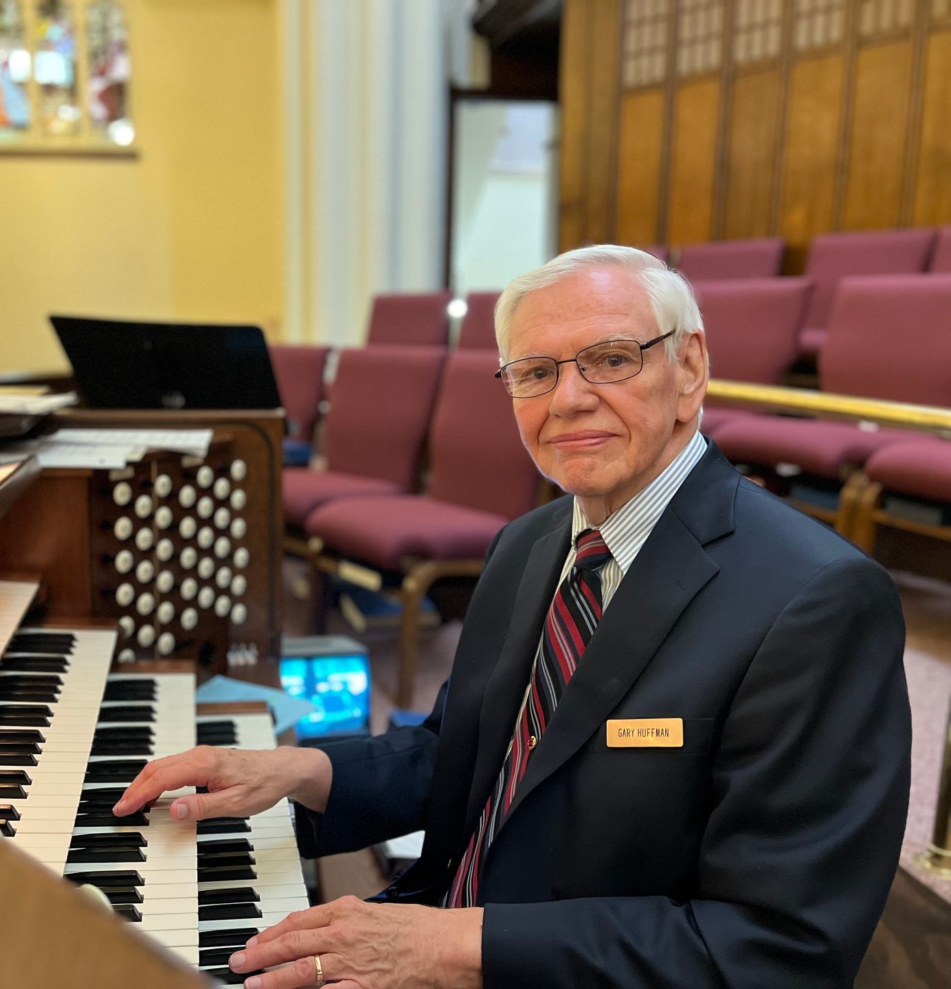 Man playing a pipe organ in a church, seated by the keyboards and smiling at the camera