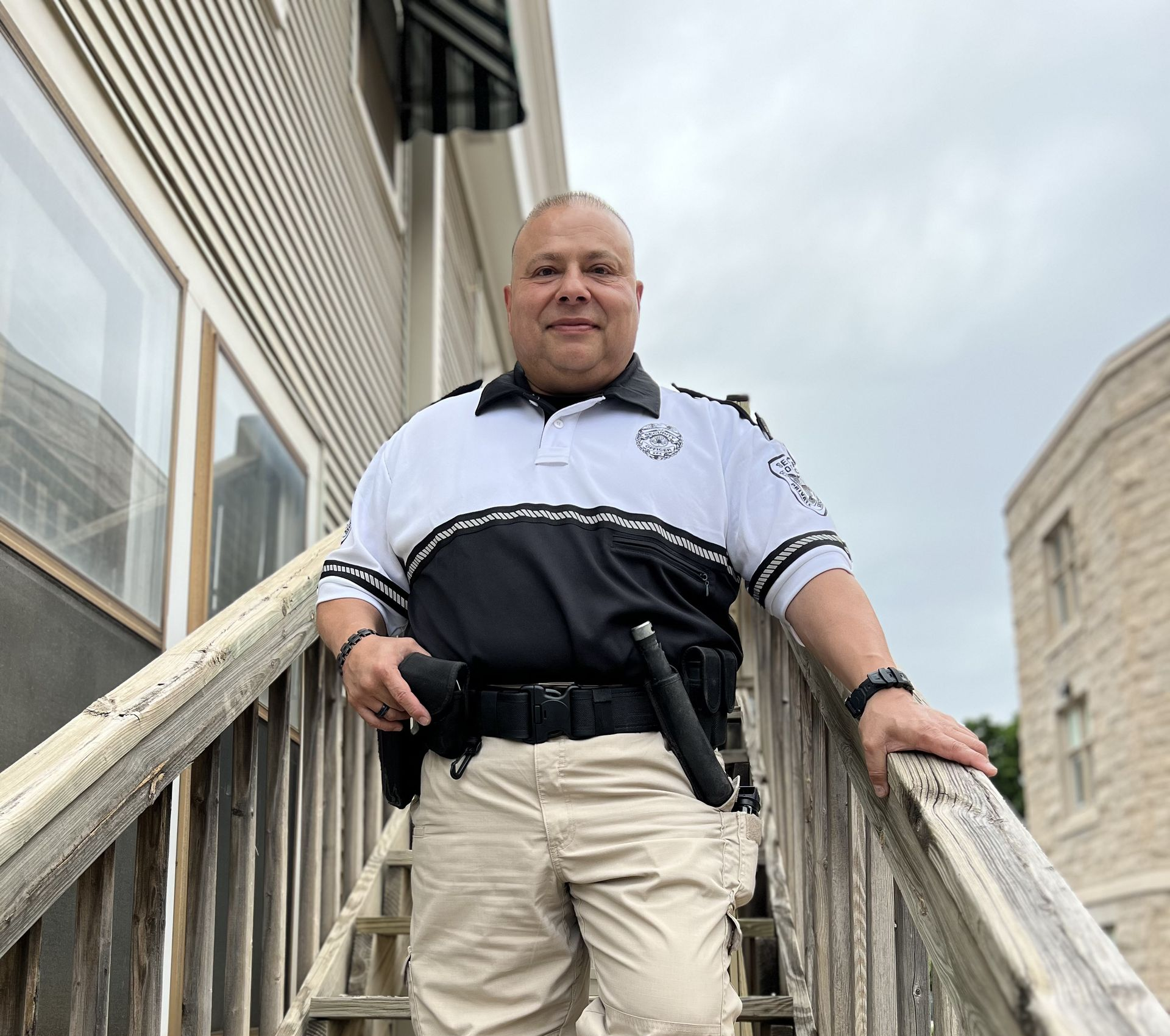Man standing on outdoor stairs beside a railing, wearing a black-and-white uniform and beige pants.