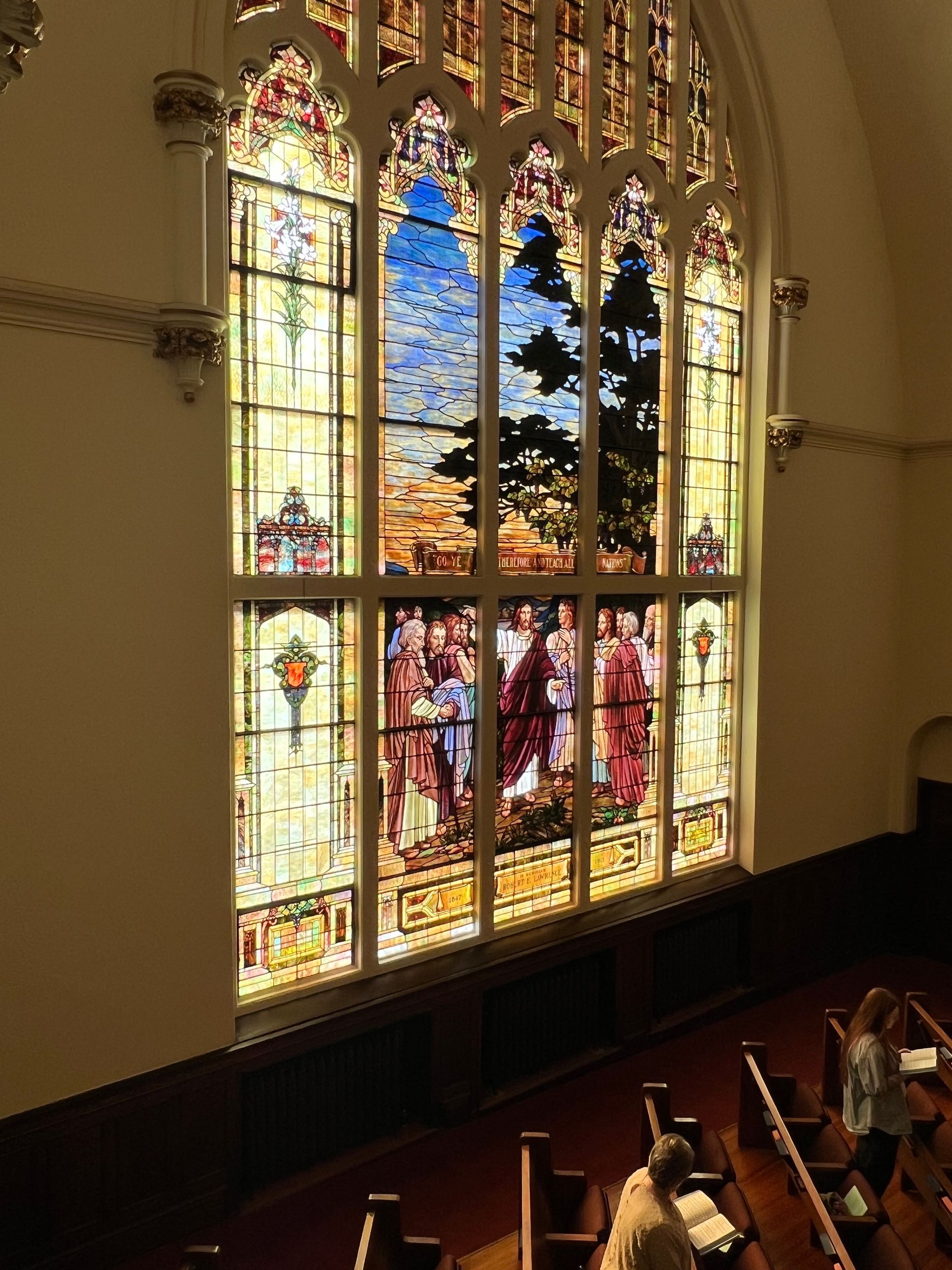 Stained-glass church window glowing with colorful biblical scenes above wooden pews