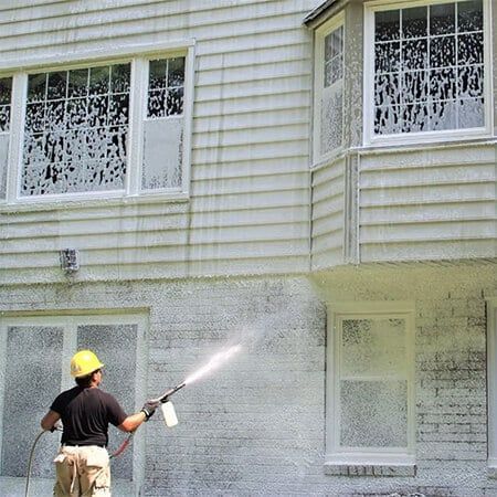 A person in a hard hat power-washes the exterior wall of a two-story home.