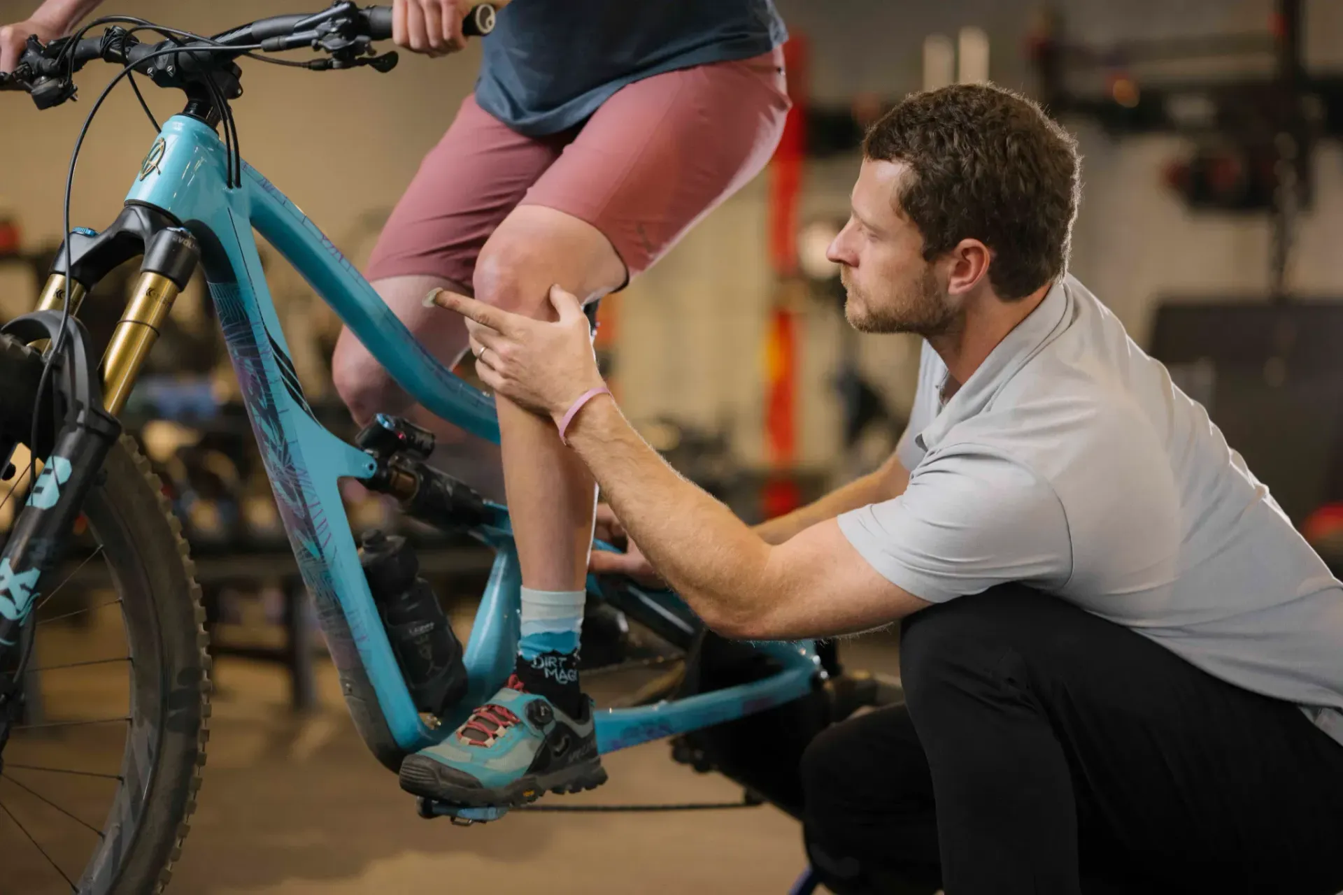 Mechanic adjusting a blue bicycle while a rider sits on it in a workshop