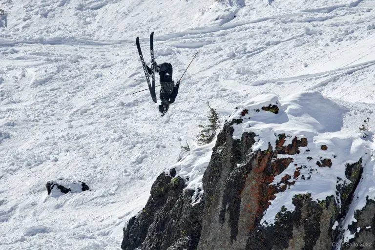 Skier midair above a snowy cliff, descending a steep mountain slope