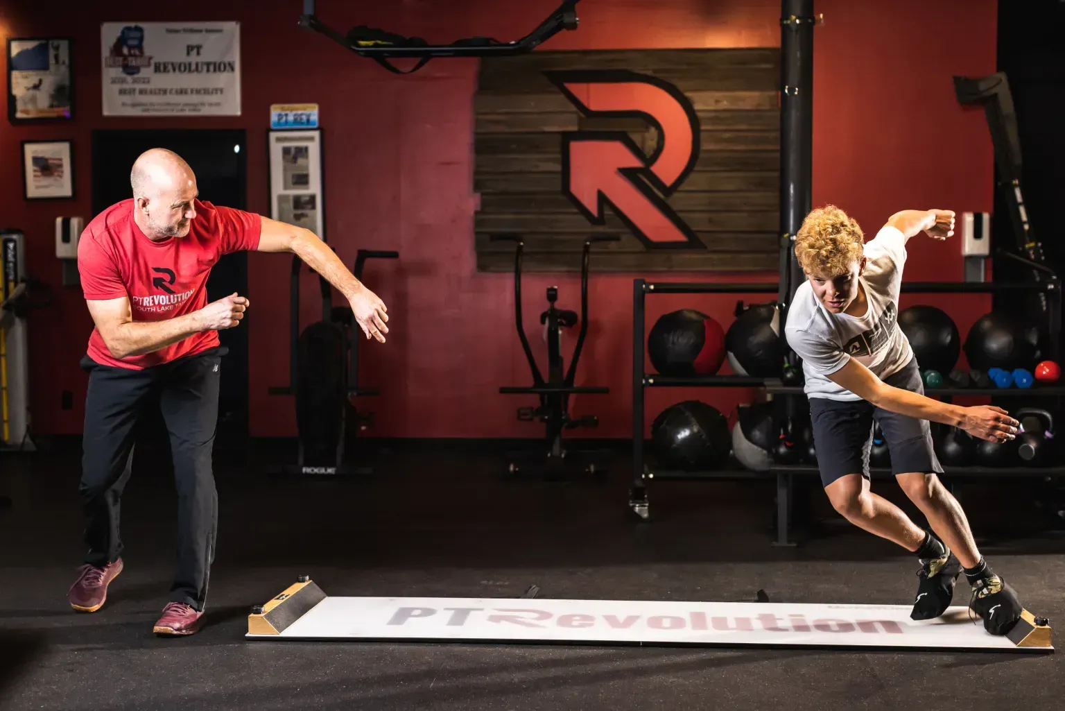 Two athletes doing balance training drills in a gym, reaching forward over a mat at PT Revolution.