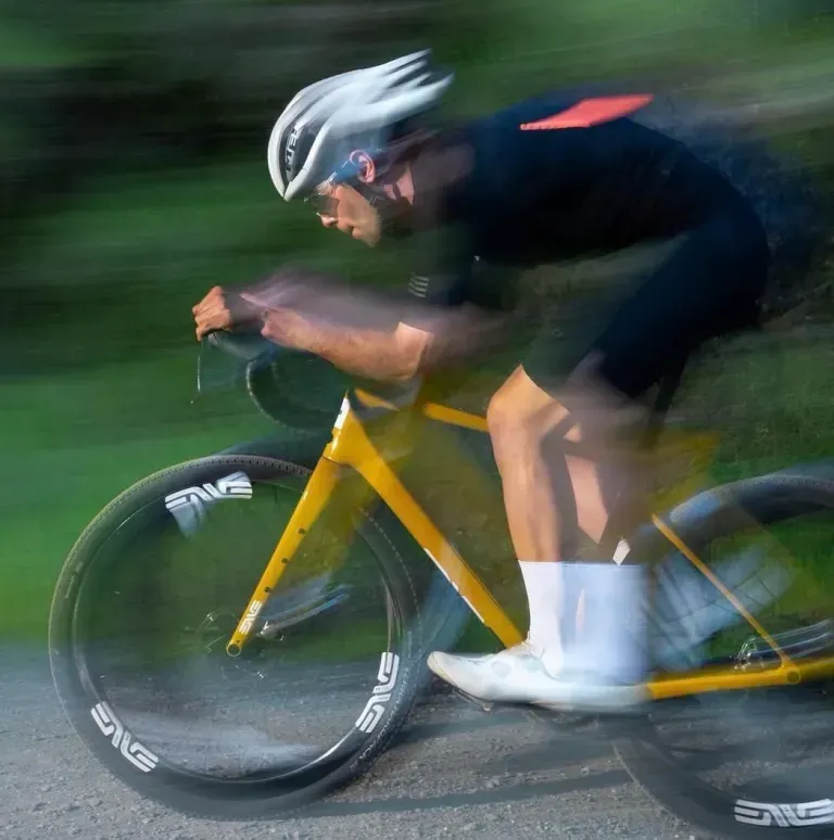 Cyclist in white helmet racing on a yellow bike, blurred in motion on a road or trail