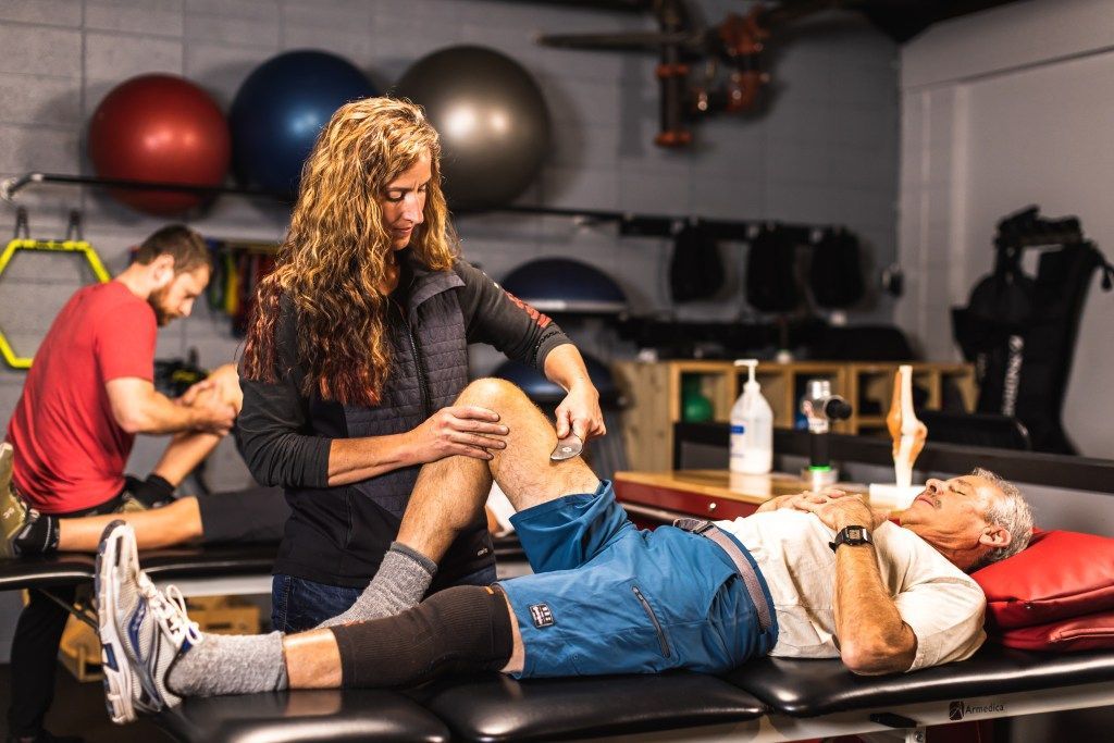 Trainer assisting a client with a leg stretch on a gym treatment table at PT Revolution, with exercise balls in the background