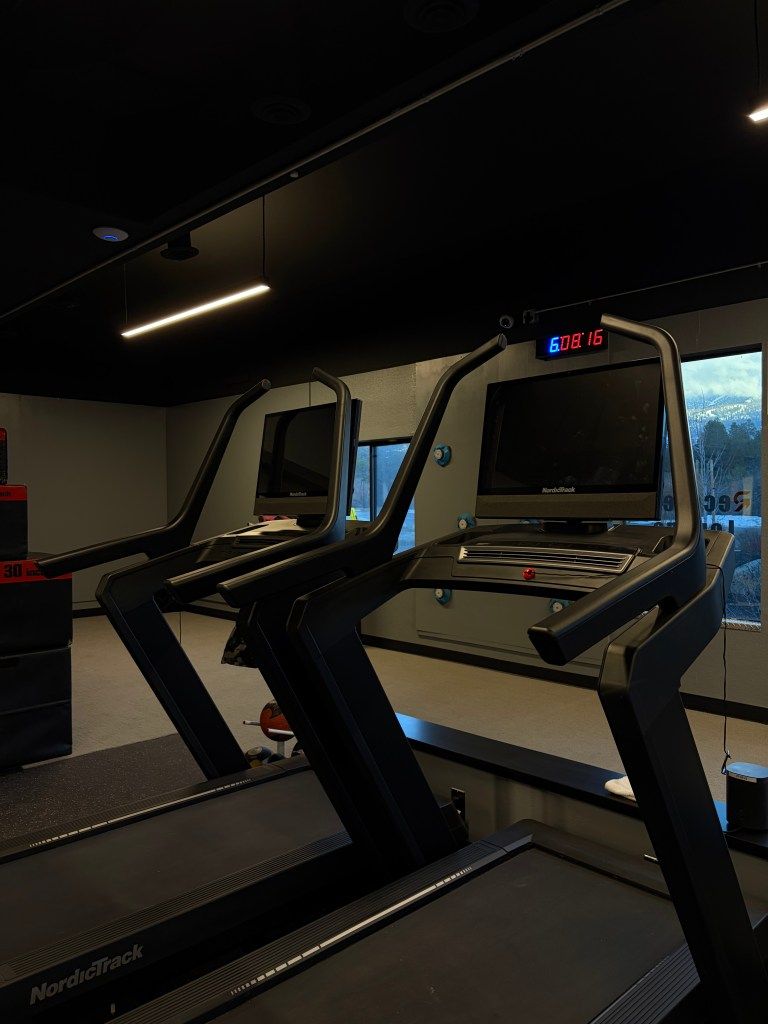 Indoor gym with two treadmills, dark walls, and a lit display near a window