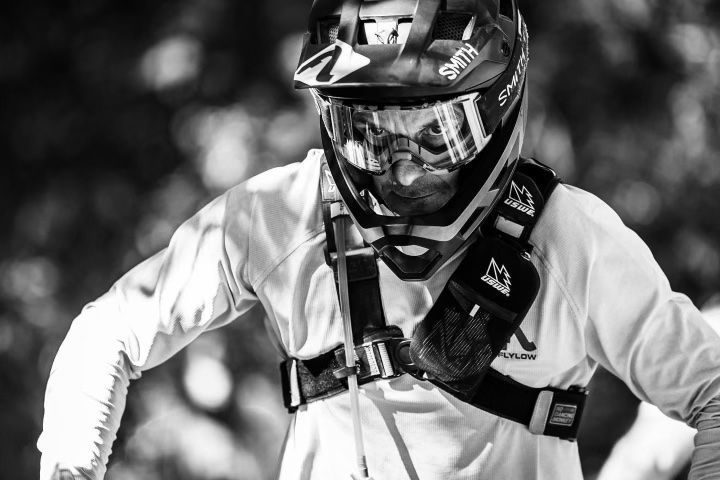 Mountain biker in helmet and goggles, leaning forward with chest protector, in black and white.