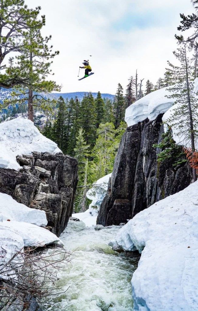 Snowy mountain river gorge with pine trees and a kayaker airborne above the rapids