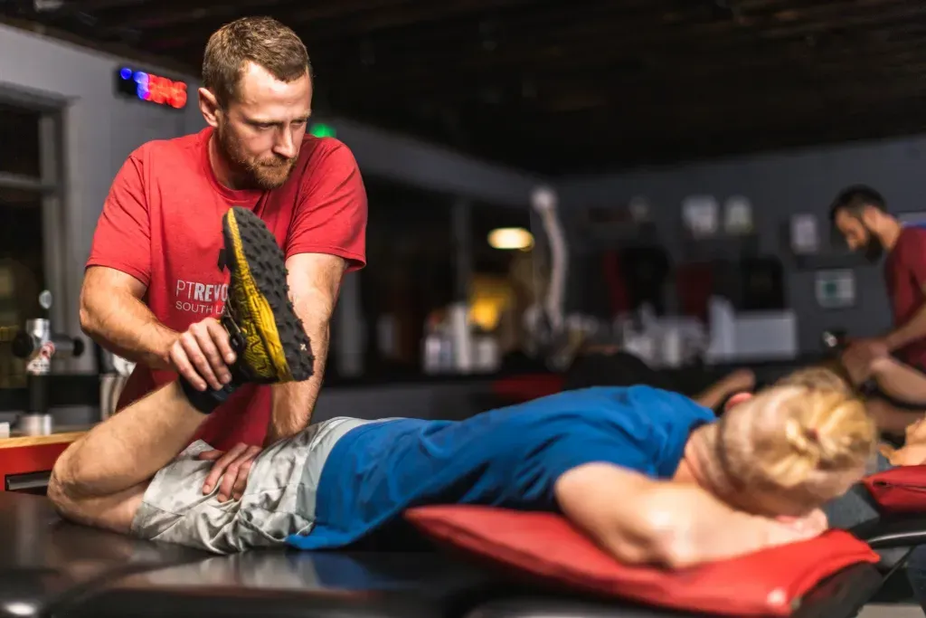 Trainer stretching an athlete’s leg at PT Revolution on a red mat in a gym, using a black-and-yellow pad