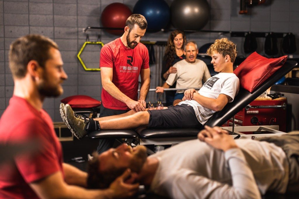 People receiving massage therapy in a gym, with therapist working on a client's legs at PT Revolution.
