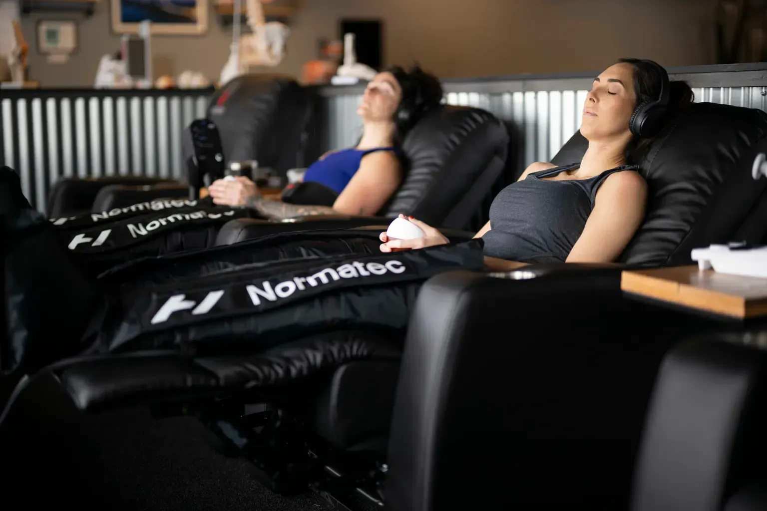 Two people reclining in black massage chairs in a dim relaxation room