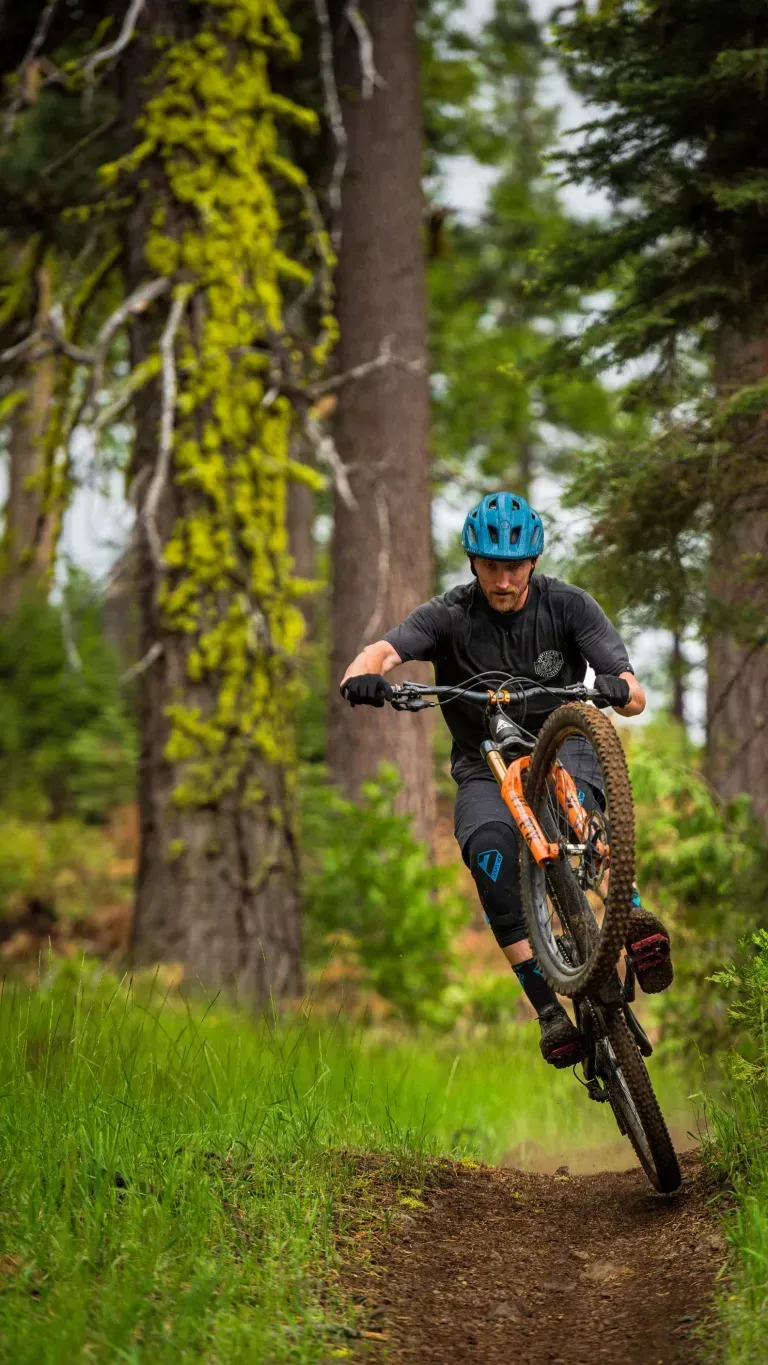 Mountain biker in a blue helmet riding a muddy trail through a forest.