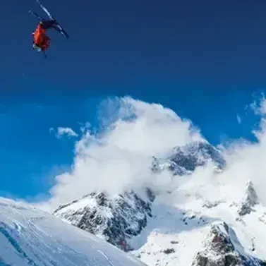 Helicopter flying above snowy mountain peaks under a clear blue sky