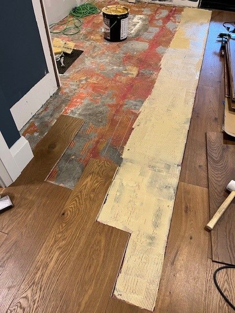 Wood planks are being glued to a floor with adhesive, showing the ongoing installation process in a room.
