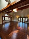 A bright, open room with polished wood floors, high vaulted ceilings with exposed wood beams, and large windows.