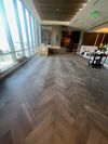 A modern, high-rise room with dark herringbone wood flooring, large floor-to-ceiling windows, and minimalist decor.