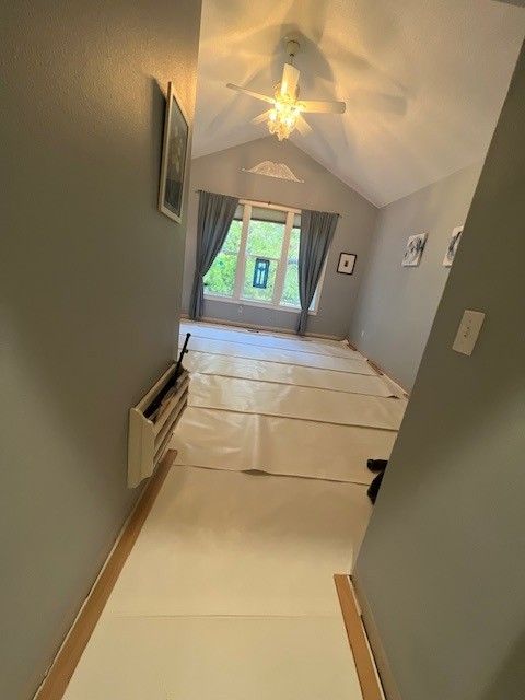 A view down a hallway into a room with gray walls, a ceiling fan, and paper floor protection covering the floor.