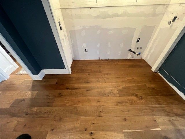 A room featuring dark blue walls, baseboard trim, and newly installed wide-plank wood flooring in front of a drywall area.