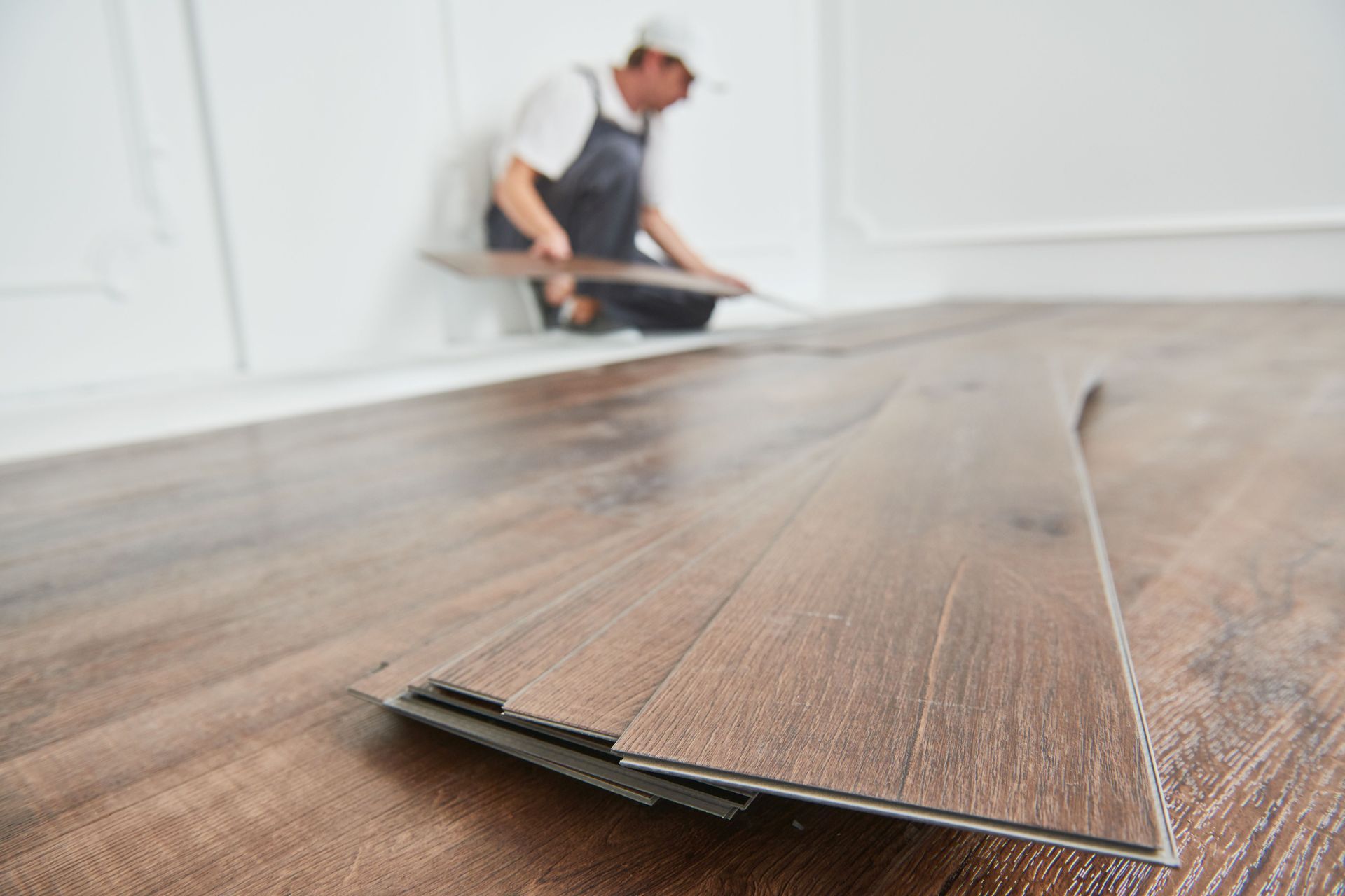 A professional installing dark brown wood-look vinyl flooring in a brightly lit room.