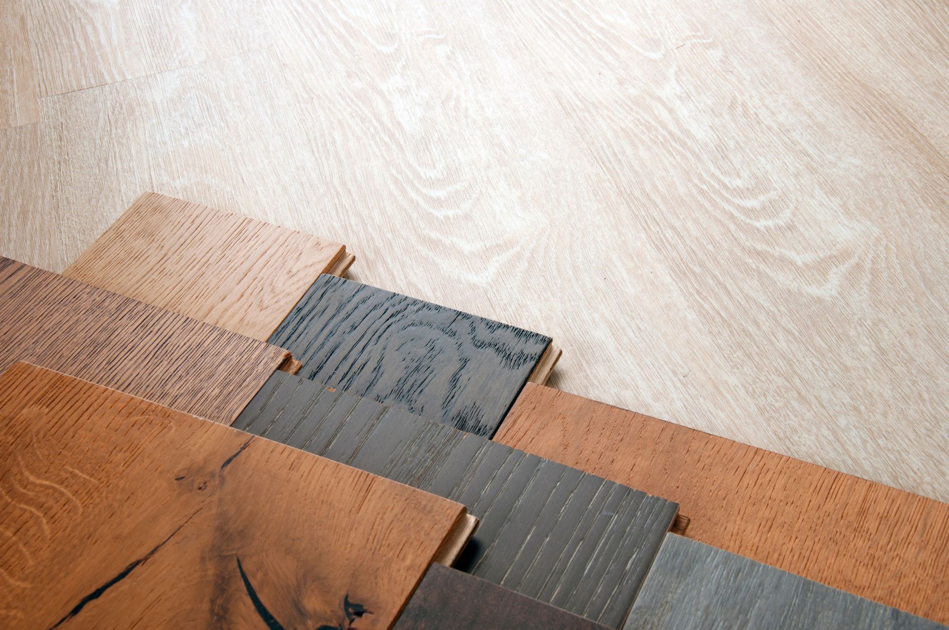 Sample wood flooring planks in various stains and textures laid out against a light wood floor background.