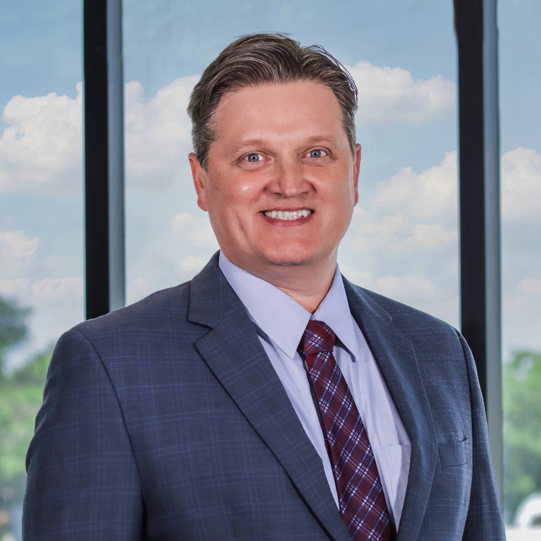 A man in a suit and tie is smiling in front of a window.