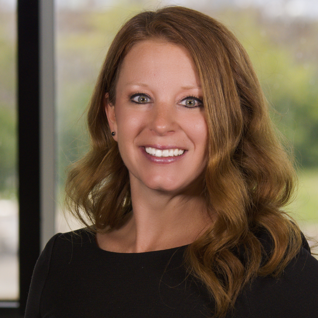 A woman with long brown hair is smiling in front of a window.