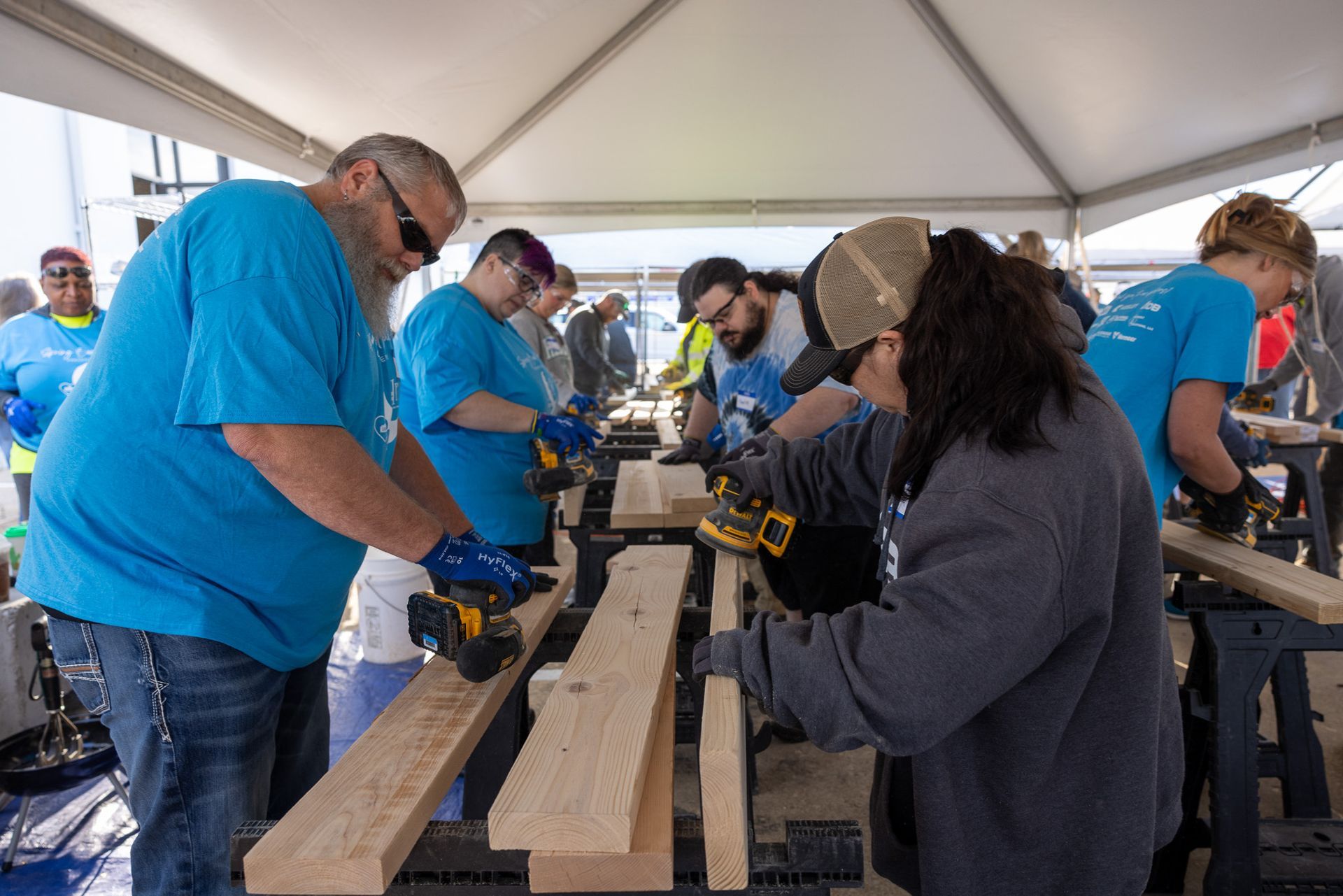 A group of people are working on wooden boards under a tent.