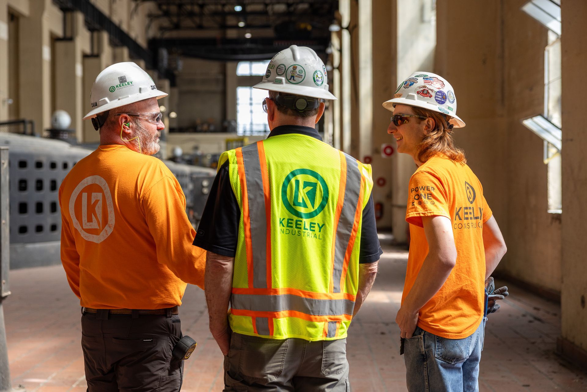 Three construction workers wearing hard hats and safety vests are standing next to each other in a building.