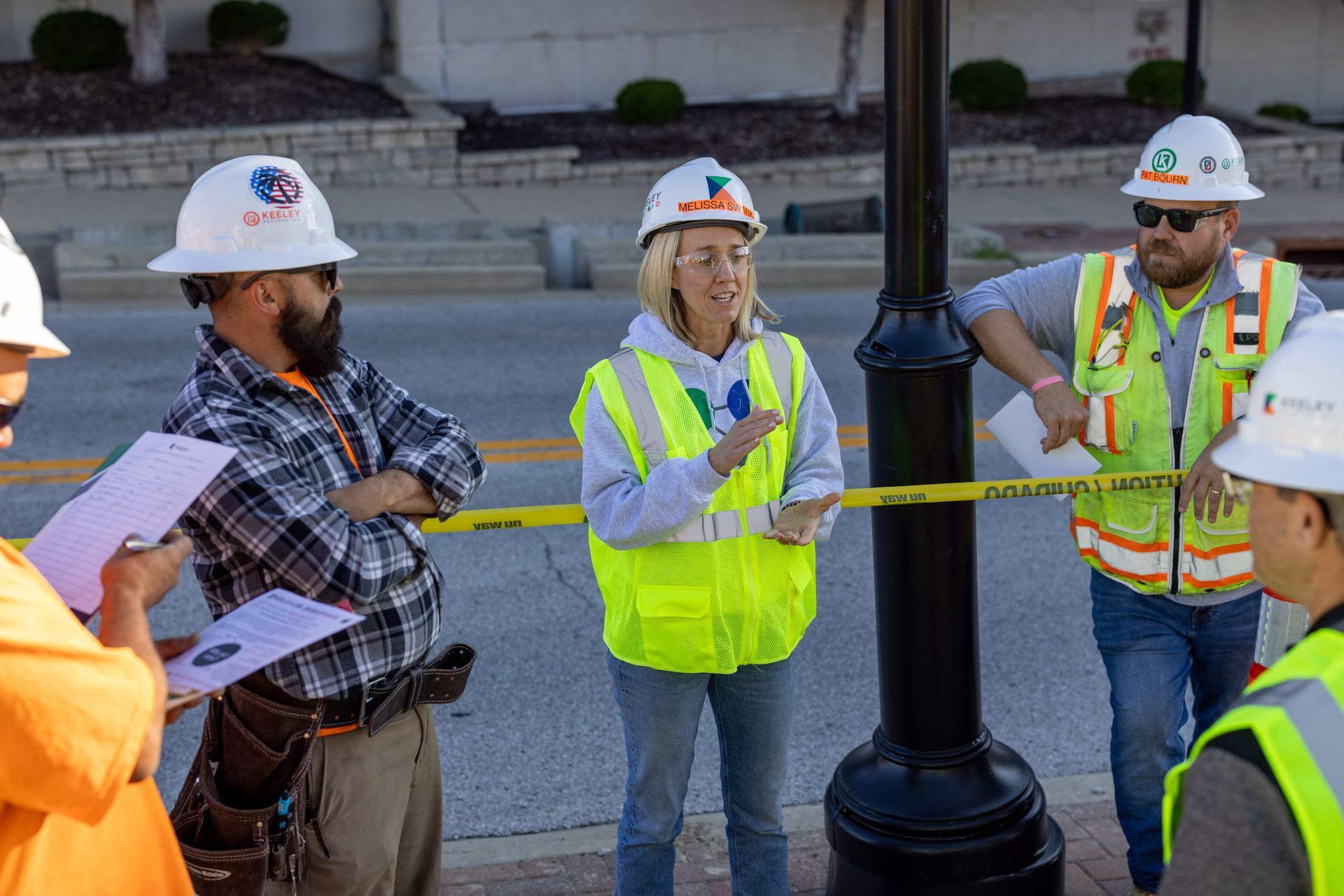 A group of construction workers wearing hard hats and safety vests are standing around a pole.