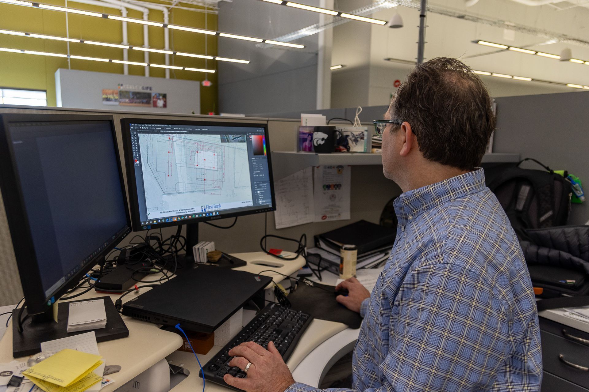 A man is sitting at a desk in front of two computer monitors.