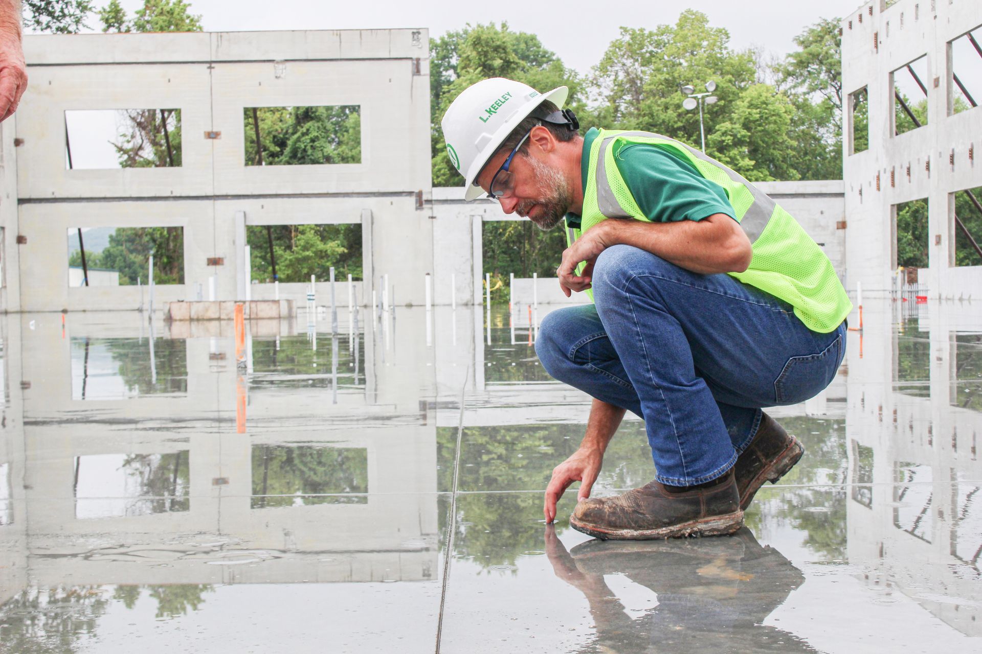 A construction worker is squatting down on a wet floor.