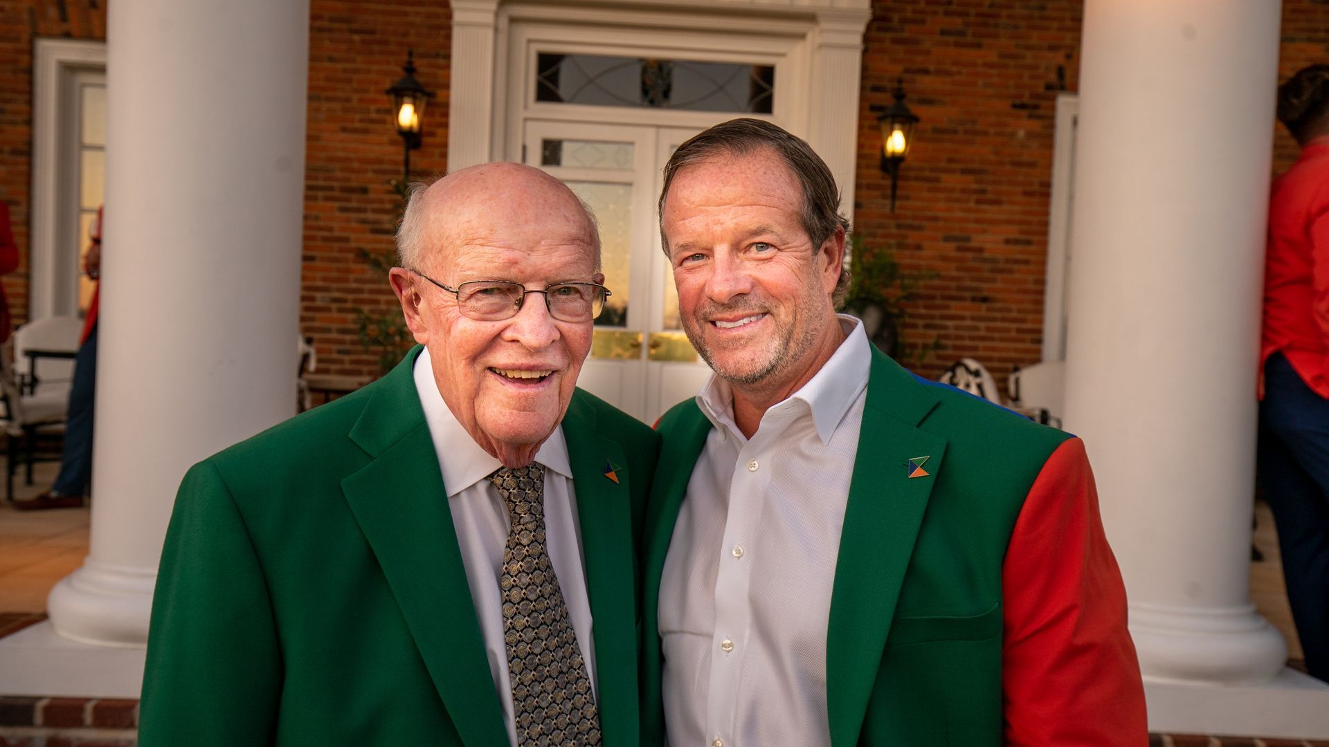 Two men are posing for a picture together in front of a brick building.