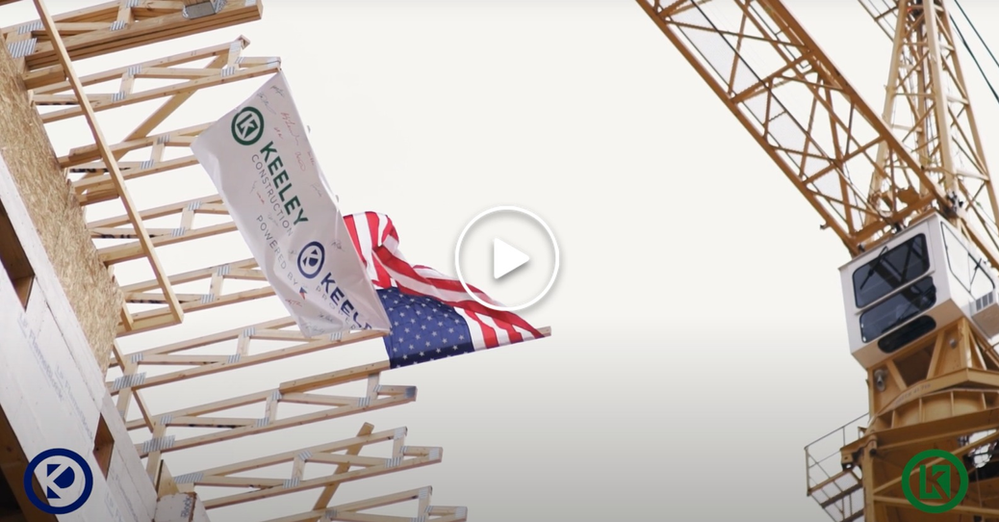 An american flag is flying in front of a construction crane.