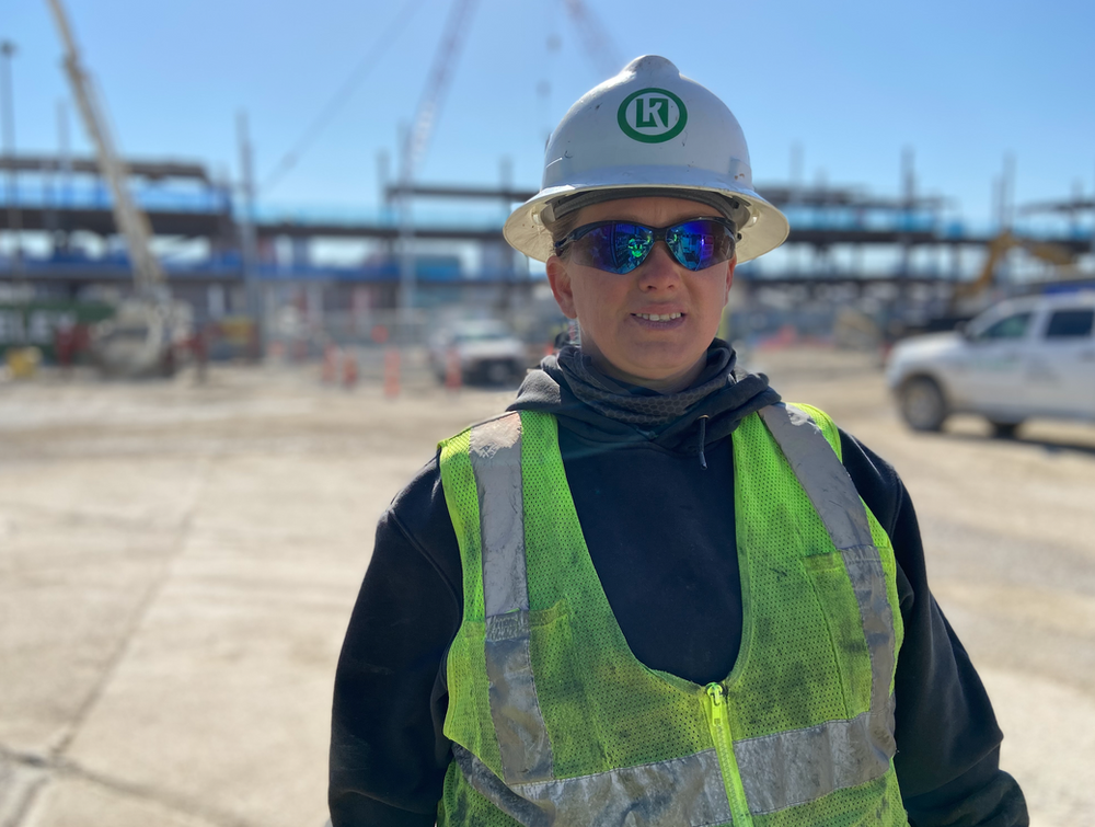 A man wearing a hard hat and sunglasses is standing in front of a construction site.