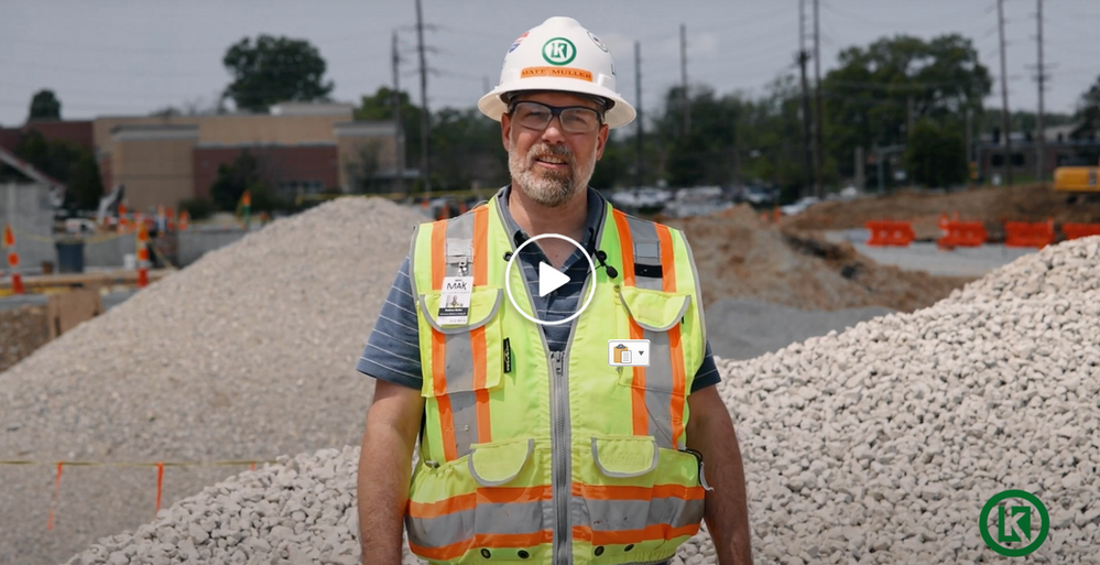 A man in a hard hat and vest is standing in front of a pile of gravel.