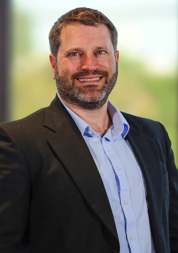 A man in a suit and blue shirt is smiling for the camera.