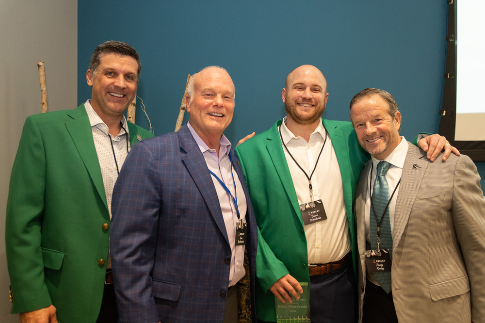 A group of men in suits and green jackets are posing for a picture.