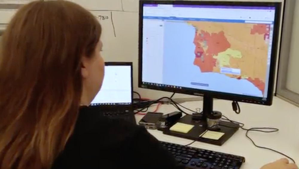 A woman is sitting at a desk looking at a computer screen.