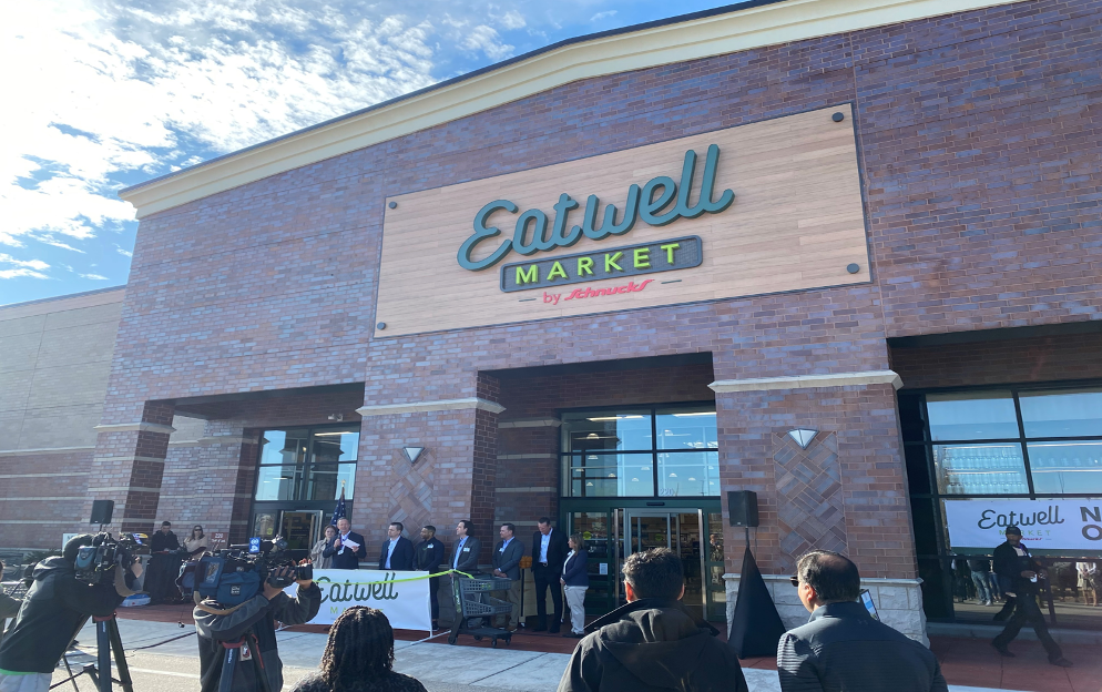 A group of people are standing outside of an eatwell market.