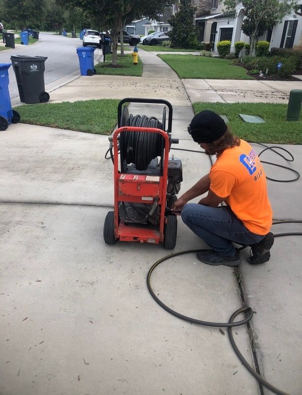A man in an orange shirt is working on a machine on the sidewalk.