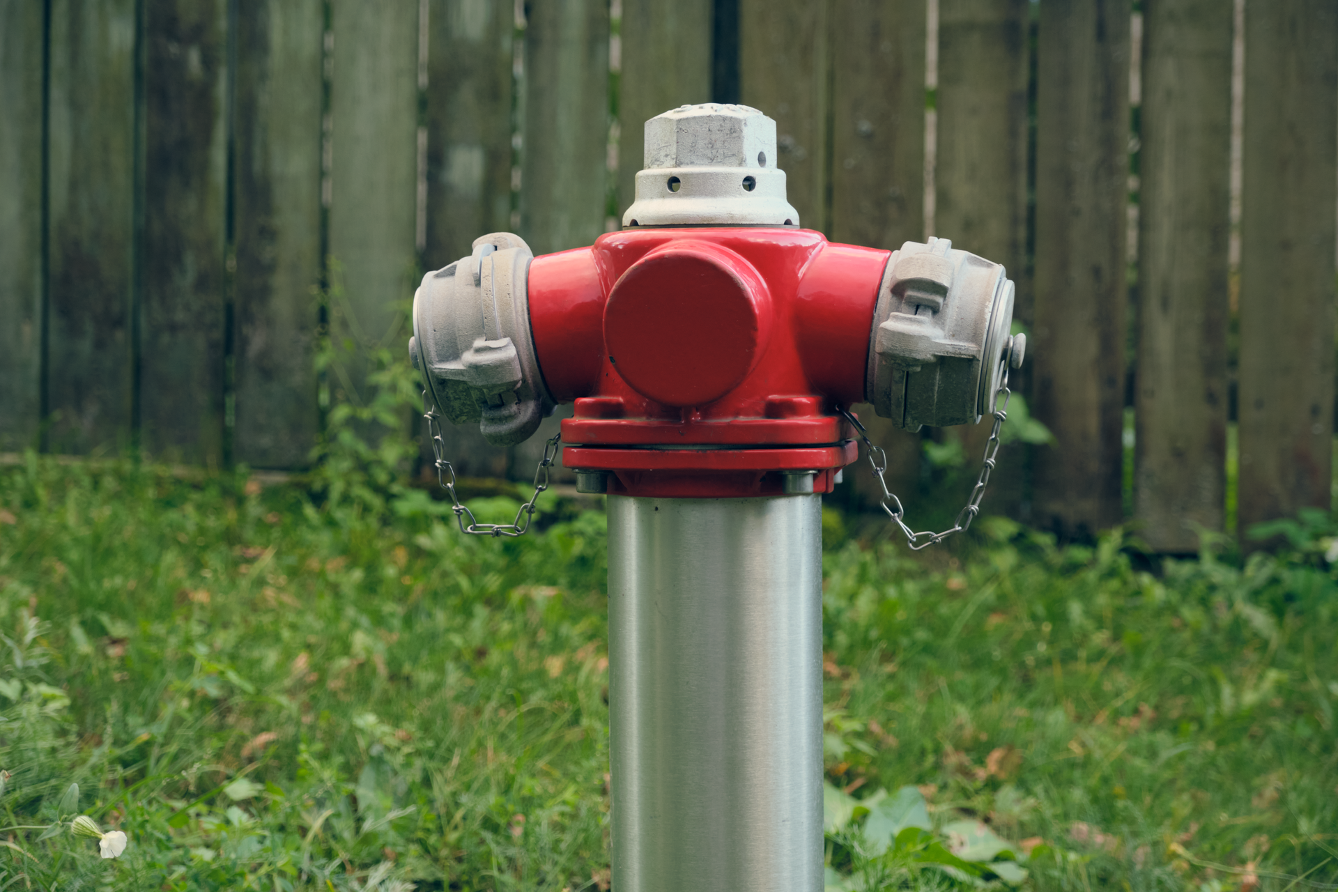 Red fire hydrant on a metal post in front of a wooden fence and green grass.
