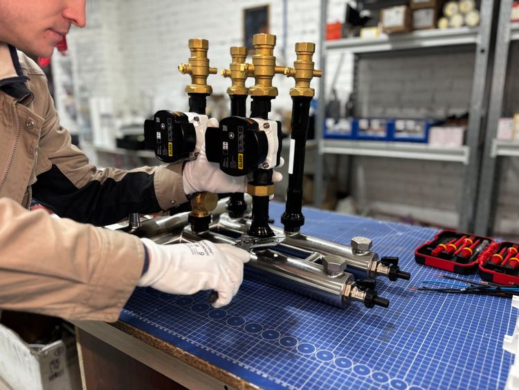 Technician assembling brass valve components on a blue workbench in a workshop