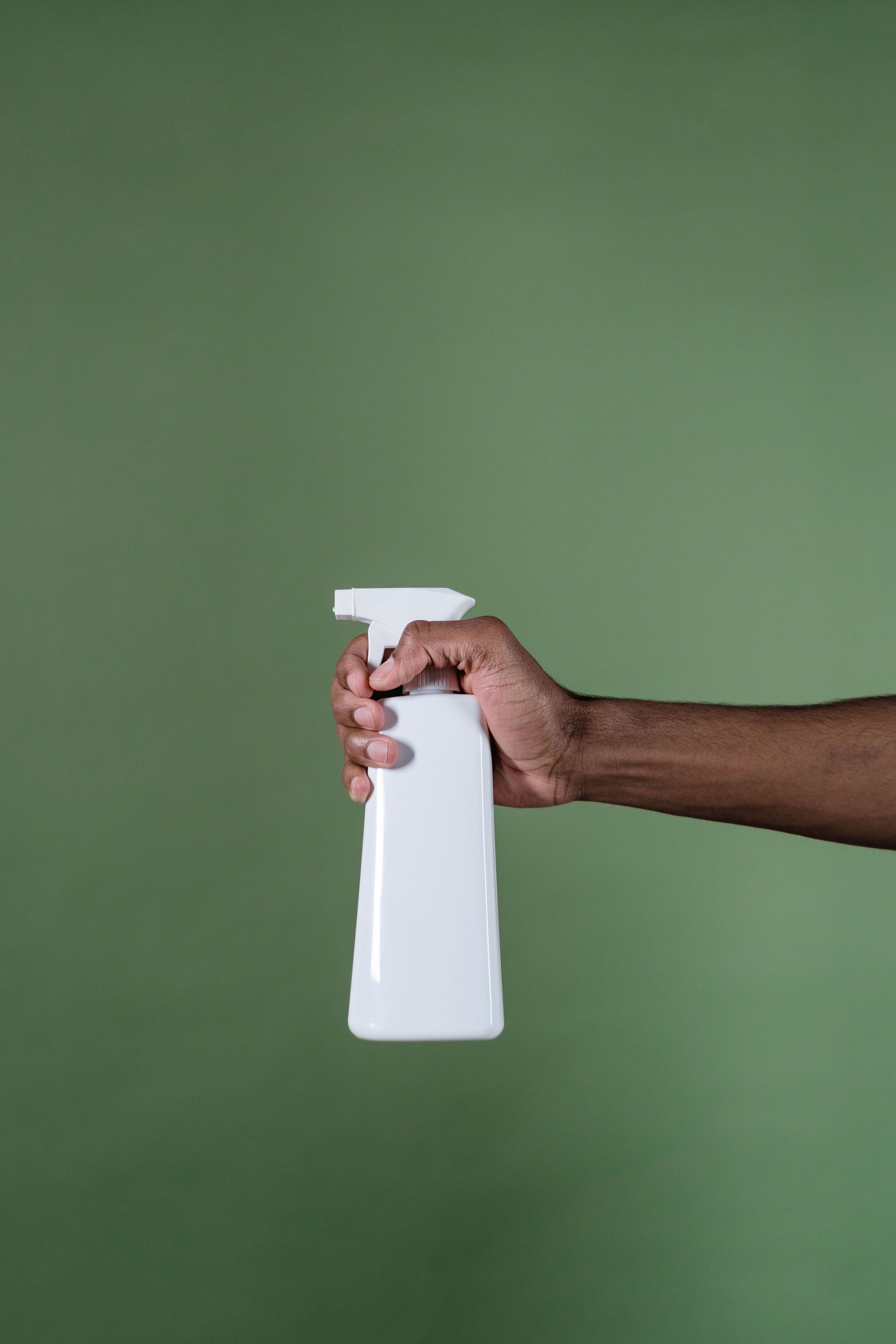 Hand holding a white spray bottle against a plain green background
