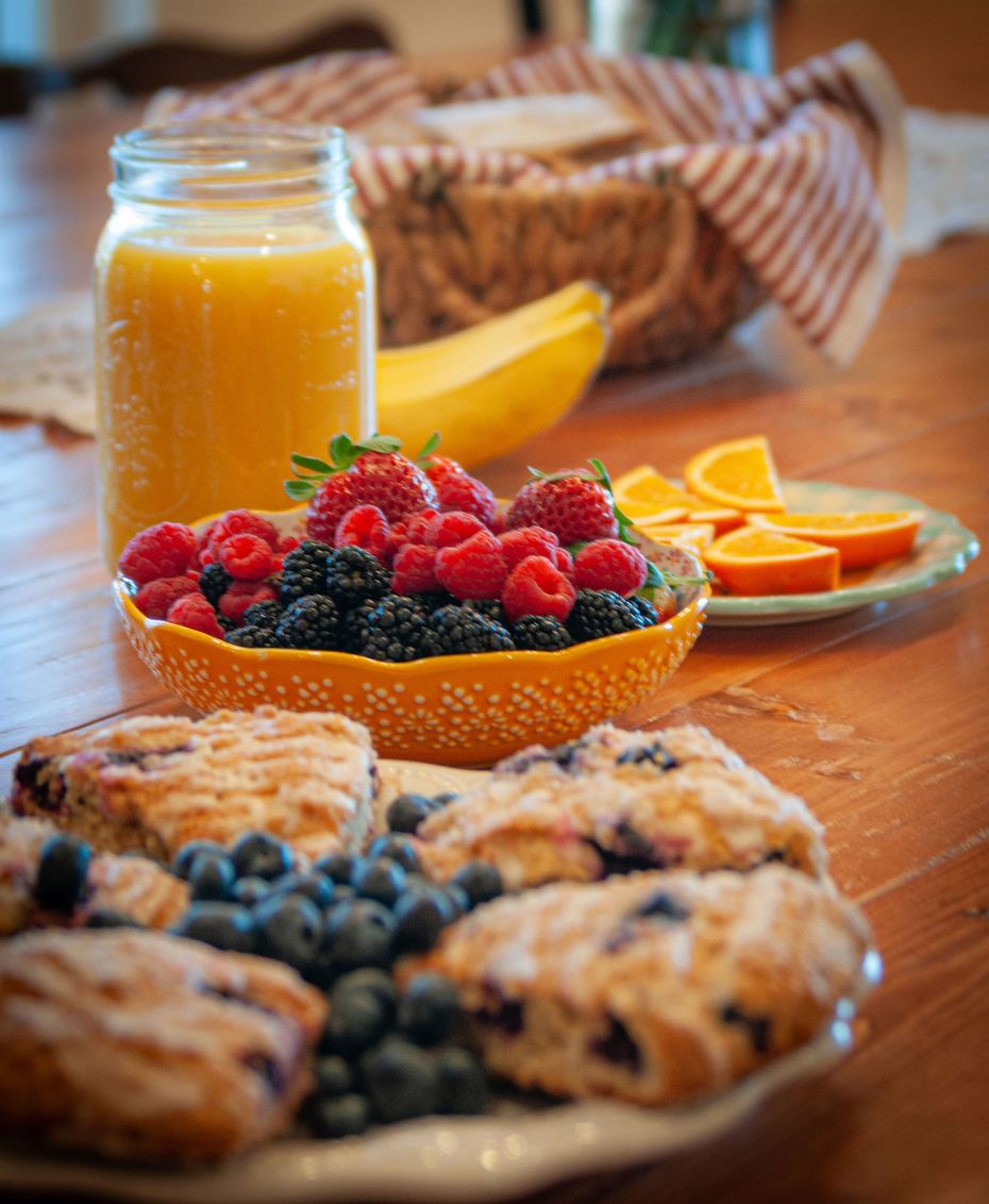 Breakfast spread with berry pastries, bowl of mixed berries, orange juice, banana, and orange slices on a table