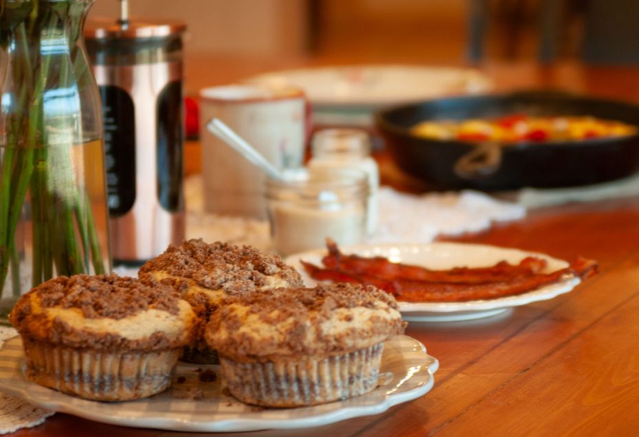 Desserts and breakfast dishes on a wooden table with cups, in a warm indoor setting