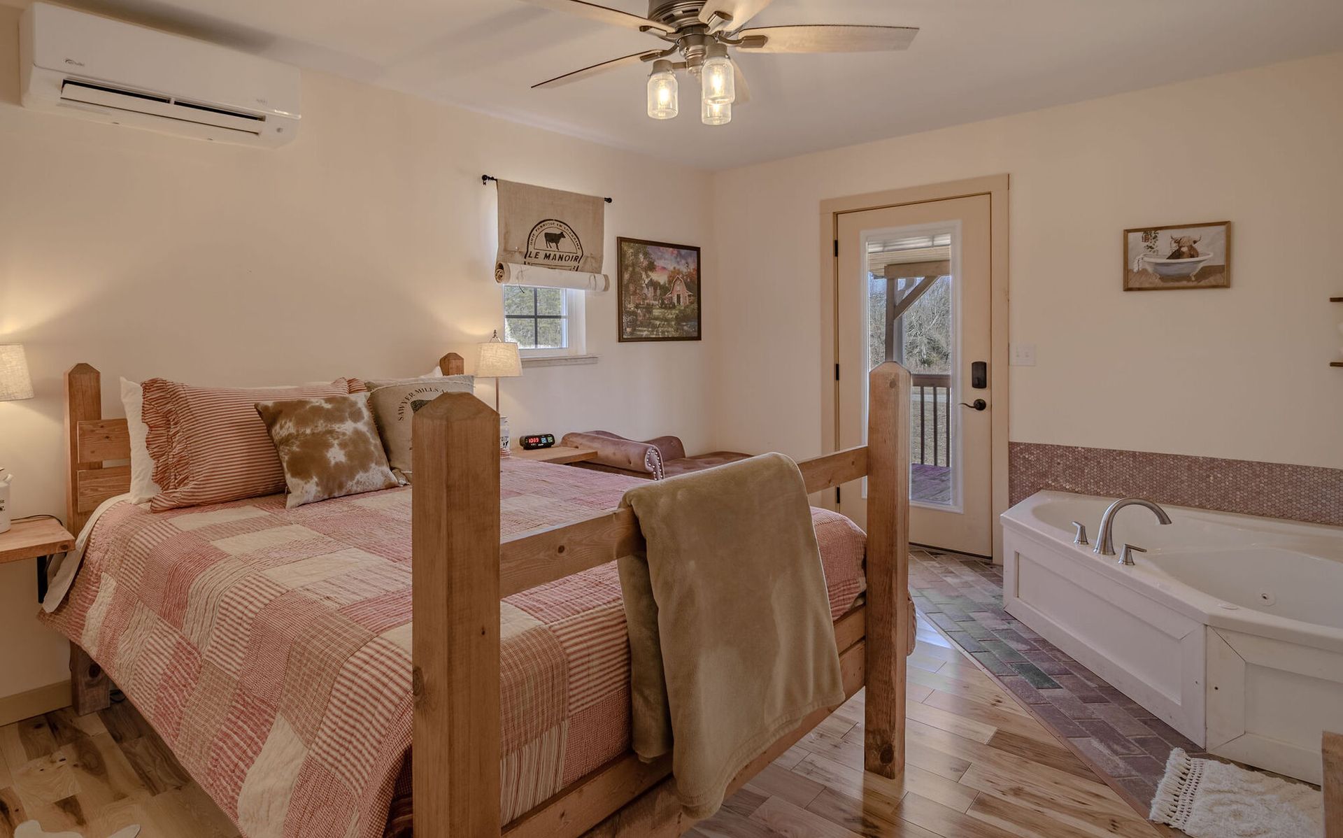 A cozy bedroom featuring a wooden four-poster bed with a patterned quilt, a whirlpool tub, and a door leading outside.